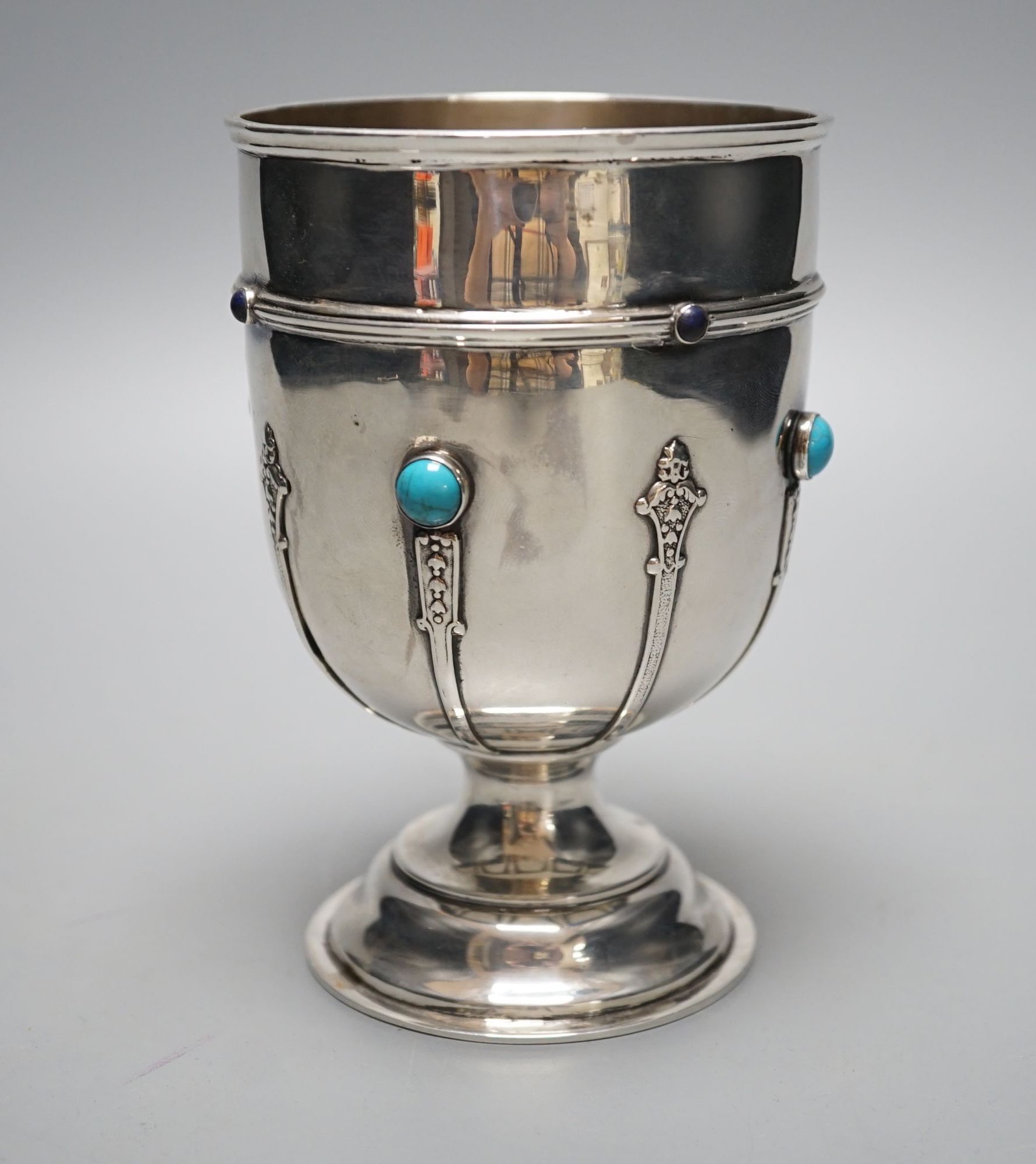 A George V silver goblet or pedestal cup with inset cabochon turquoise and cabochon lapis lazuli, with engraved crest and strapwork decoration, Henry Moreton, Chester, 1913, 13.6cm, gross weight 7oz.